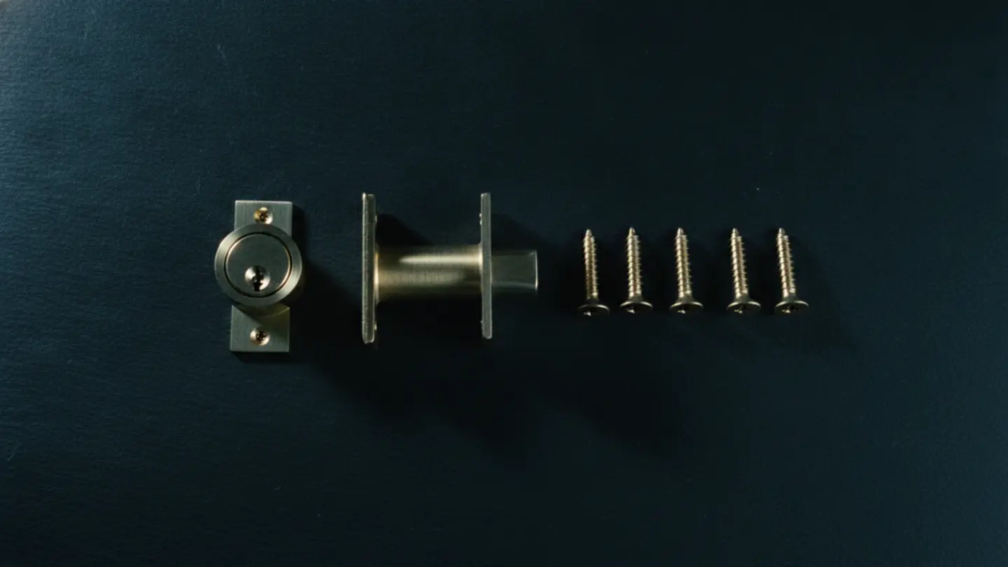 A brass deadbolt with its strike plate and mounting screws laid out for fitting, lit cold cyan on dark slate