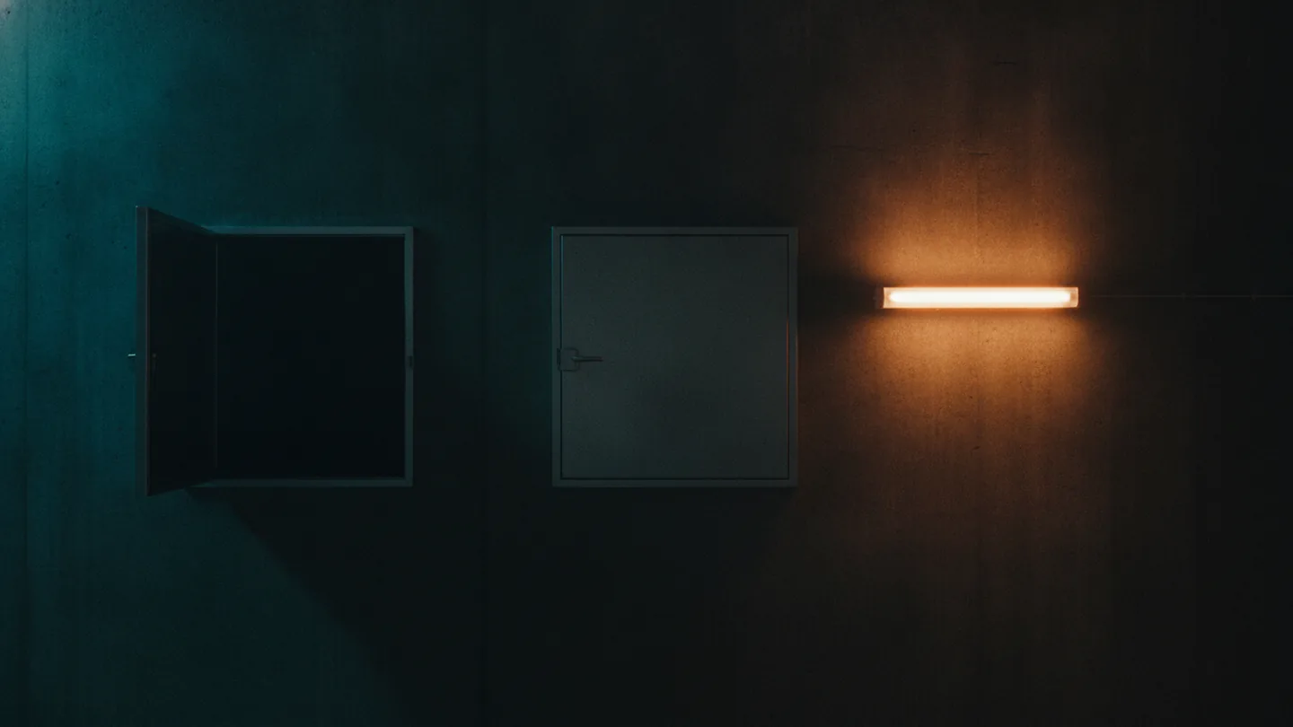 An open steel hatch beside a sealed one in a dark concrete plant room wall, lit cold cyan