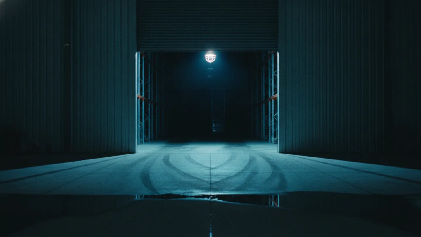 Half-raised roller door on a dark warehouse spilling cold cyan light