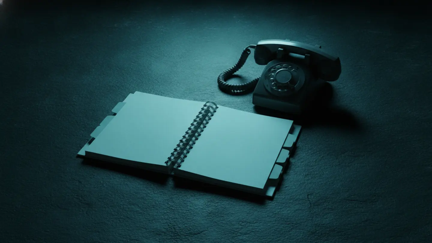 Spiral-bound emergency response plan with tabbed pages lying open beside a corded telephone on dark slate, lit cold cyan